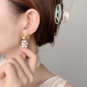 Elegant gold bow earrings with clustered pearl pendants shown on a model's ear