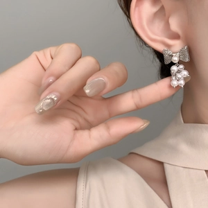 Elegant silver bow earrings with cluster pearl drops shown on model's ear in high detail