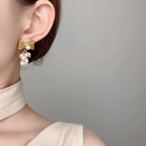 Close-up of elegant gold bow earrings with white pearls worn on a model's ear