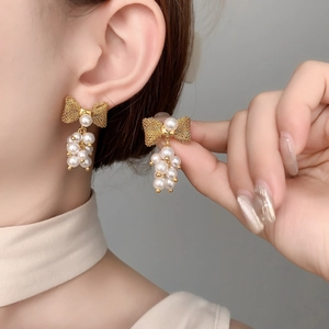 Close-up of elegant golden mesh bow earrings with dangling white pearl clusters