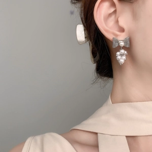 Close-up of elegant bow-shaped metal earrings with white pearl cluster tassels