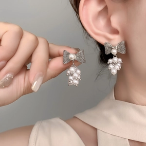 Close-up of elegant bow pearl drop earrings with woven texture on model's ear