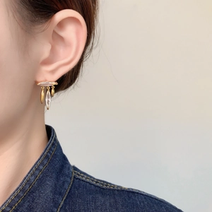 Close-up of gold leaf fringe earrings with zircon inlay worn by a model in denim