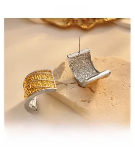 Macro detail of mixed-metal C-shape earrings with gold lava texture and silver outer frame