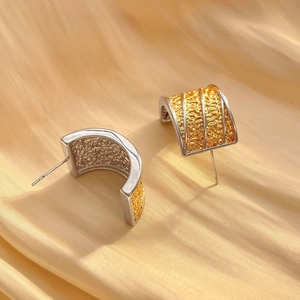 Macro shot of two-tone C-shape earrings with textured gold lava pattern and silver borders
