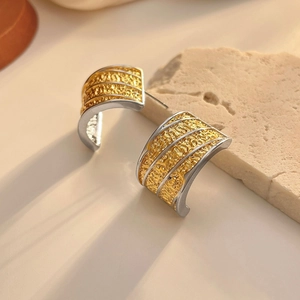 Macro detail of C-shaped earrings with dual-tone gold and silver lava rock textures