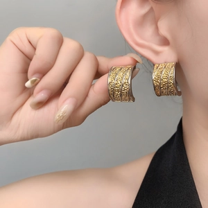 Macro detail of wide C-shaped gold earrings with unique volcanic lava texture