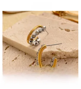 Detail of geometric C-shaped earrings in two-tone gold and silver metal cube design