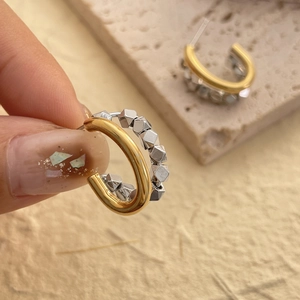 Macro shot of two-tone geometric earrings with gold outer ring and silver cube beads
