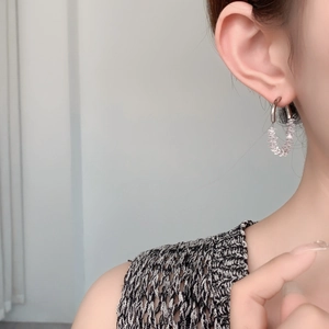 Close-up of sparkling silver hoop earrings with clear zircon crystals on model's ear