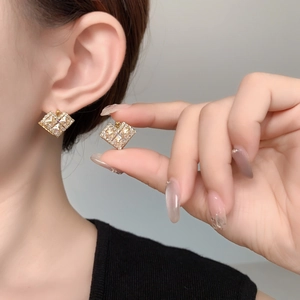 Close-up of gold geometric cubic zirconia hoop earrings worn on a model's earlobe