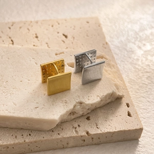 Detailed close-up of square metal cufflinks in gold and silver on stone display pedestal