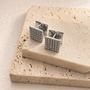 Detail of square silver cufflinks with pavé-set zircons on a textured stone surface
