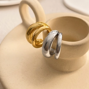 Close-up of interlocking C-shaped gold and silver earrings on a ceramic rim