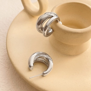 Detail showing the textured silver C-shape double-layer earrings on a ceramic base