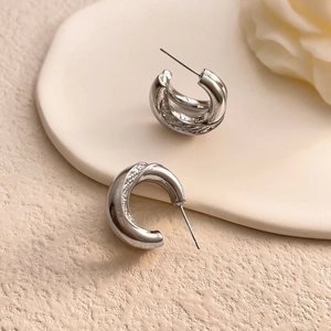 Macro shot of silver C-shaped hoop earrings featuring polished finish and woven texture details