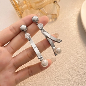 Dettaglio di orecchini pendenti in argento con zirconi e perle tenuti in mano