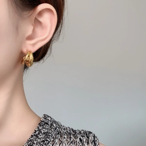 Close-up of golden multi-layer C-shaped geometric hoop earrings worn on ear