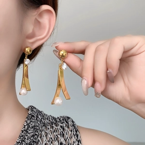 Dettaglio di eleganti orecchini pendenti dorati con borchie in zircone e perle bianche