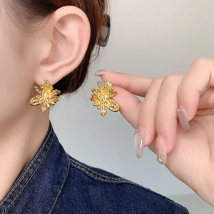 Macro detail of 18K gold plated flower earrings featuring liquid metal texture on ear