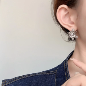 Detailed close-up of a silver flower earring with zircon center worn on earlobe