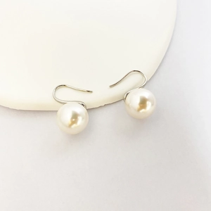 Elegant white pearl drop earrings with silver hooks displayed on white ceramic plate