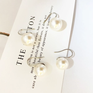 Elegant round pearl drop earrings with minimalist silver U-shaped hooks on a card