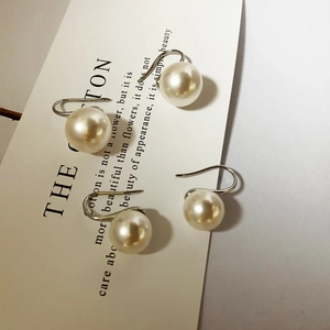 Detail view of two pairs of elegant white pearl drop earrings with silver hooks on card
