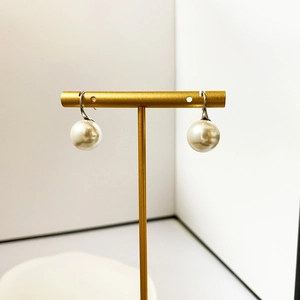 Detail view of elegant white pearl drop earrings on a minimalist gold jewelry stand