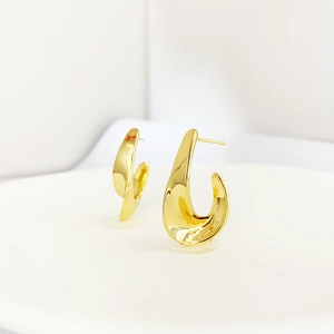 Close-up of golden sculptural twisted earrings with high-polish liquid metal texture