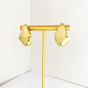 Makro-Detail von goldenen geometrischen Creolen mit polierten Facetten auf einem Ständer