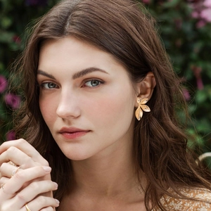 Elegant gold leaf stud earrings worn by a model in a natural outdoor garden setting