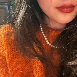 Detailopname van een parelketting op een oranje trui voor een elegante herfstlook