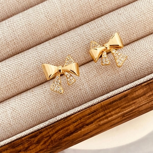 Elegant gold bow earrings with micro-pave zircons displayed in a beige jewelry box
