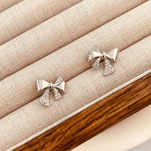 Macro shot of silver bow earrings with zircon stones on a beige velvet jewelry box
