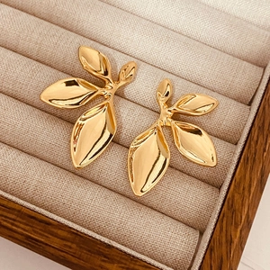 Detail shot of golden leaf-shaped earrings with mirror-polished finish in a wooden box