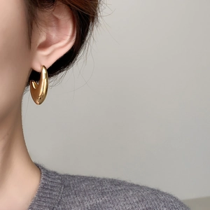 Close-up of polished C-shaped chunky gold earrings worn by a model in soft purple knitwear