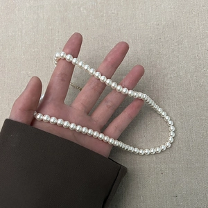 Detail van witte ronde parelketting met gouden sluiting op een getextureerde achtergrond
