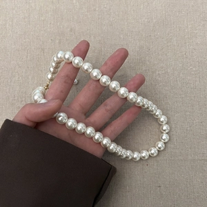Detail van een elegante witte parelketting met een gouden karabijnsluiting in de hand