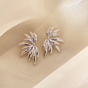 Detail of silver angel wing stud earrings with polished metallic finish on satin cloth