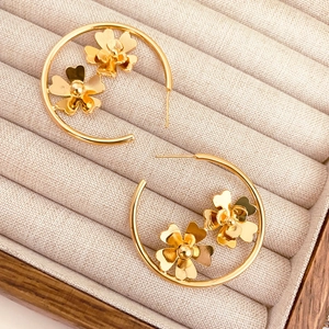 Créoles dorées avec détails floraux délicats présentées dans un écrin à bijoux beige
