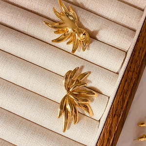 Close-up of golden angel wing earrings with feathered texture on beige velvet