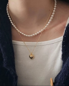 Close-up van een gelaagde parelketting en gouden hartjes hanger bij een model