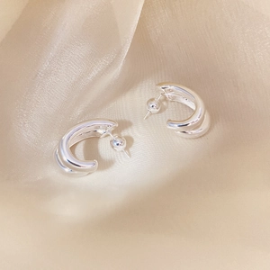 Macro detail of double-layered silver C-shape stud earrings on champagne silk fabric