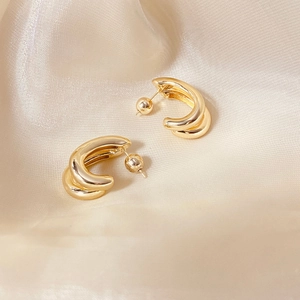 Close-up of golden double-layer C-shaped hoop earrings on beige silk fabric