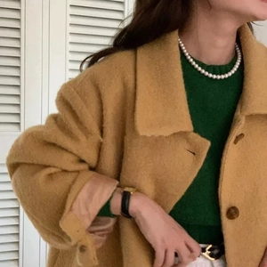 Detail van elegante parelketting met een wollen jas en een groene gebreide trui eronder