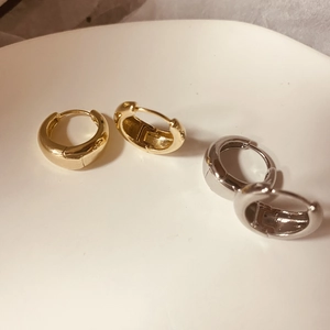 Detail van dikke goud en zilver gepolijste oorringen op een minimalistisch wit dienblad