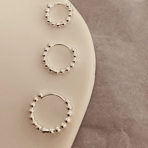 Détail de trois tailles de créoles en argent avec billes sur un support de bijoux