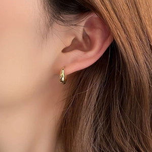 Close-up van een model met een strakke gouden druppelvormige oorbel in moderne stijl