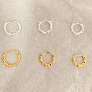 Détail de boucles d'oreilles créoles perlées or et argent en trois tailles sur marbre
